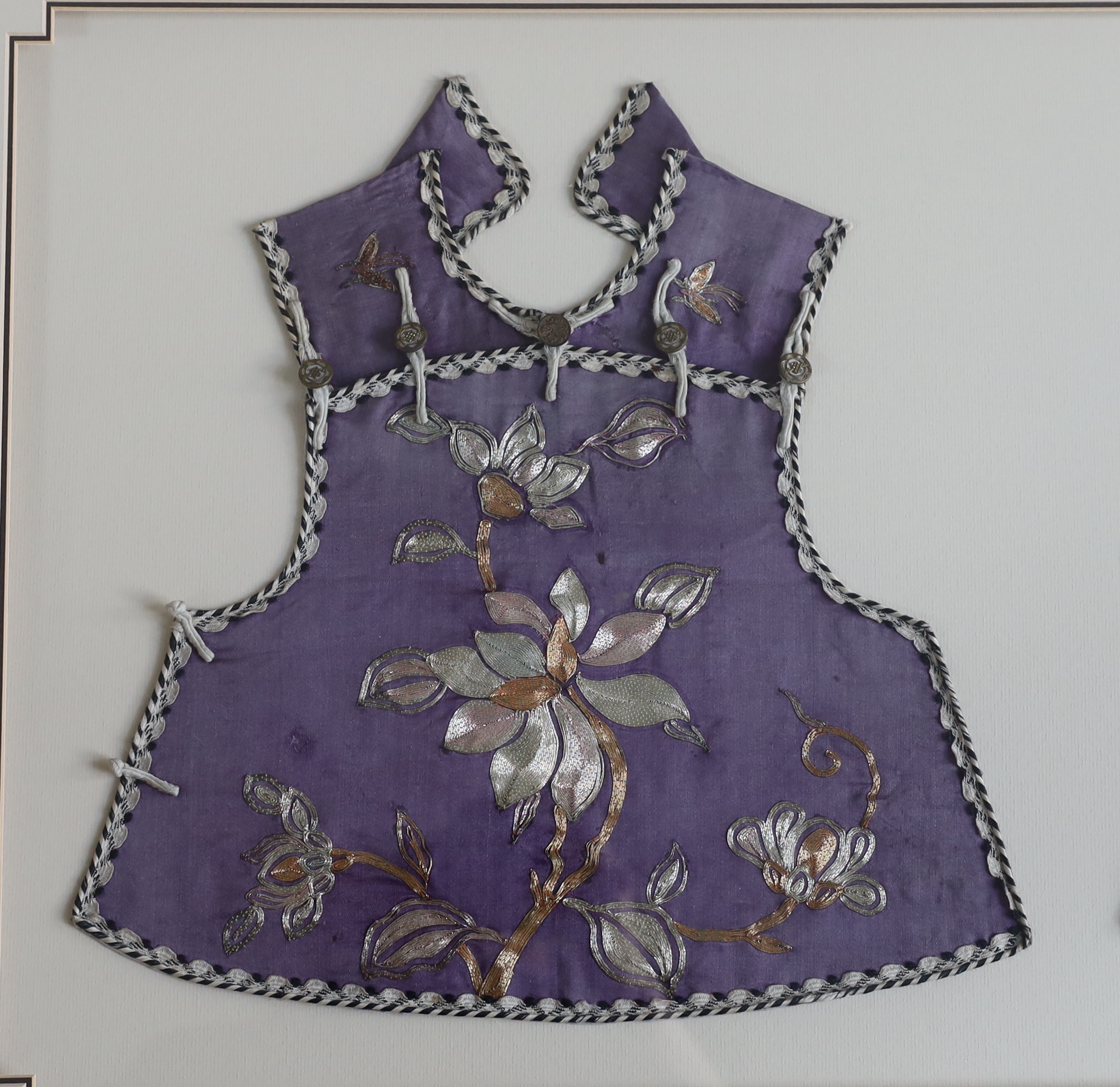 A late 19th century Chinese child’s purple silk and multi-coloured metal embroidered tabbard, front and back panels split and double mounted in one frame, 33cm wide, 37cm high